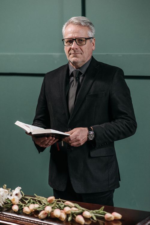 Free Senior man wearing a black suit and eyeglasses, holding a book with flowers on a table. Stock Photo