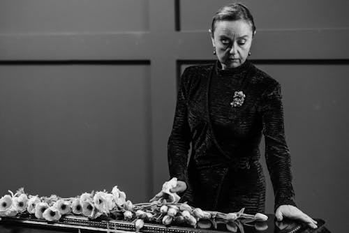 A mature woman in black attire arranging flowers with a thoughtful expression.