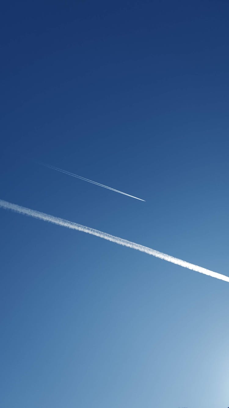 Airplanes With Condensation Trails Flying In Blue Cloudless Sky