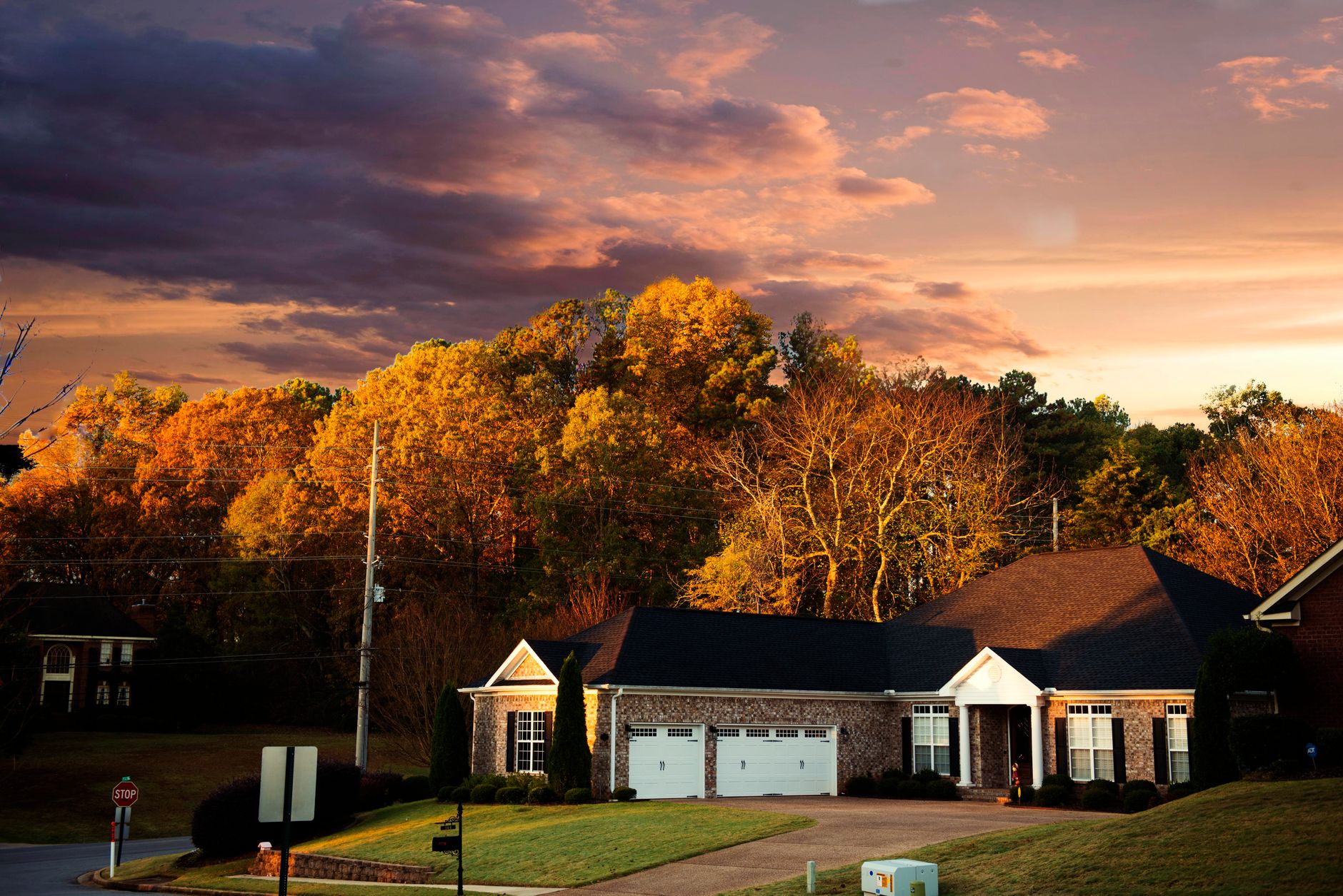 A picturesque suburban house surrounded by fall foliage under a dramatic sunset sky in Madison, AL.