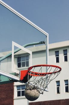 A basketball goes through the hoop outdoors in an urban setting.