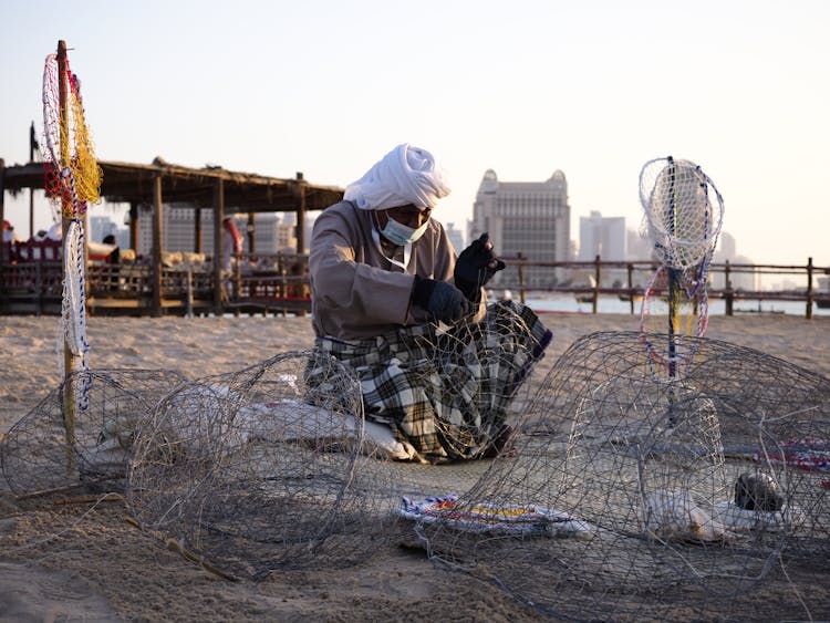 Elderly Woman Weaving A Fishing Net On A Beach 