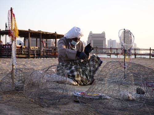 Free Elderly man crafting fishing nets on a sandy beach at sunset, showcasing traditional skills. Stock Photo