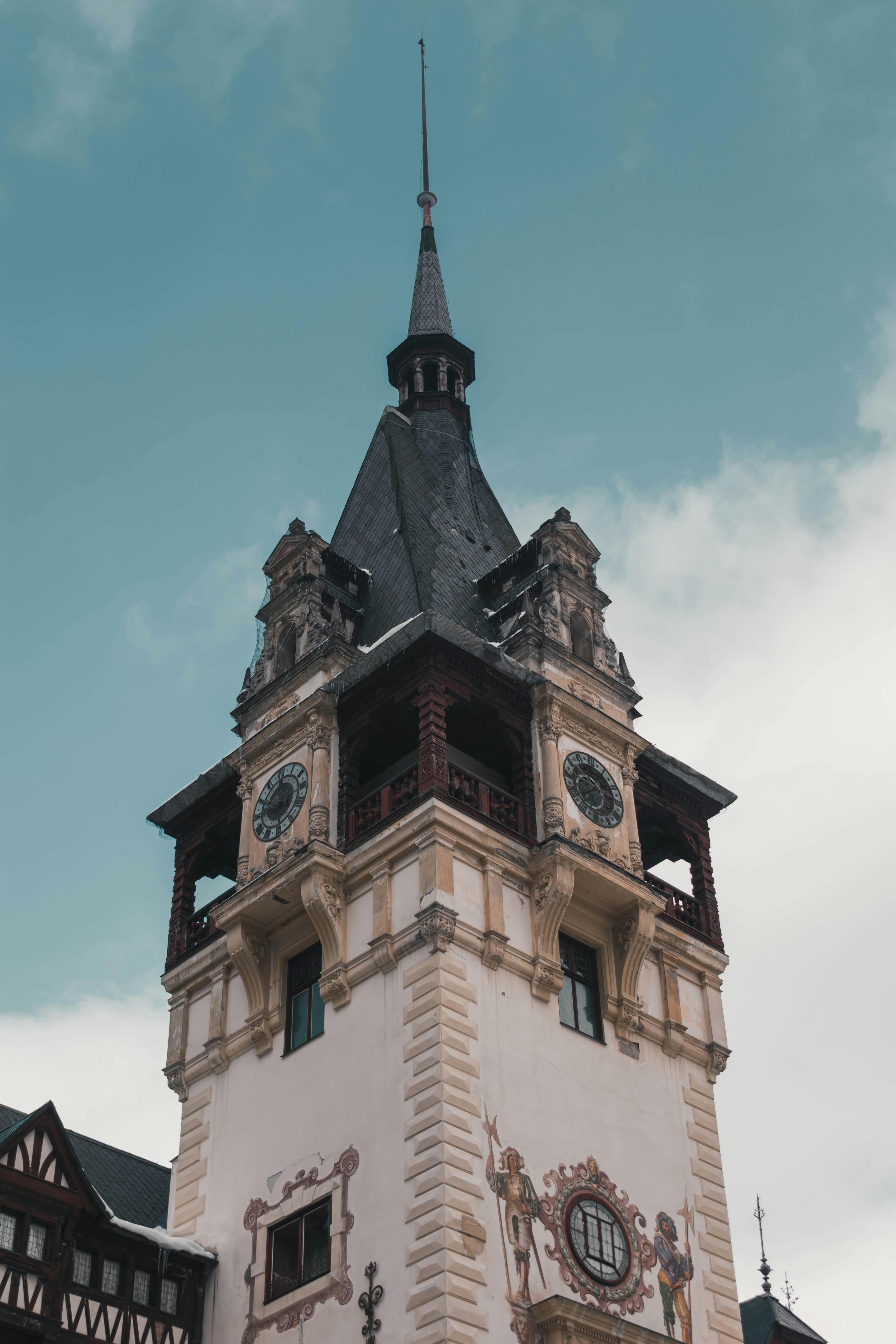 Low angle shot of Peles Castle's intricate Gothic Revival tower against a clear blue sky in Sinaia, Romania.
