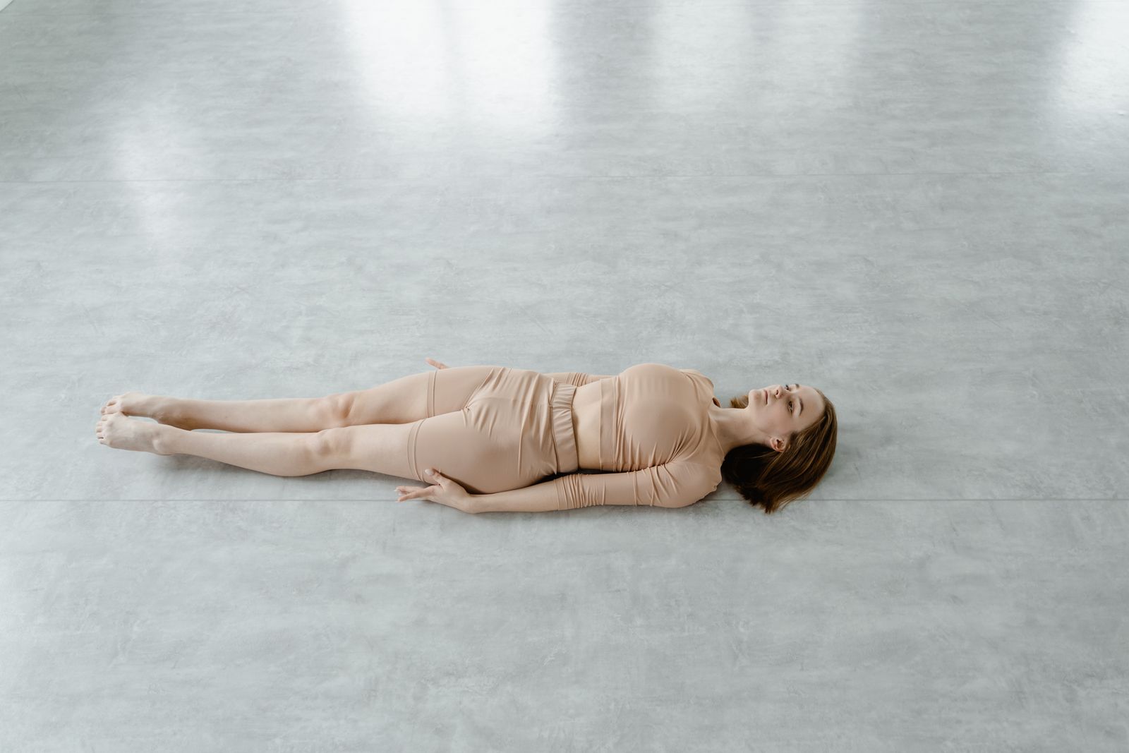 Woman lying flat on the floor with legs extended and arms relaxed in savasana relaxation pose