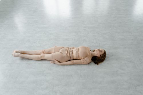 Free Woman in nude activewear lying flat on a light gray floor indoors. Stock Photo