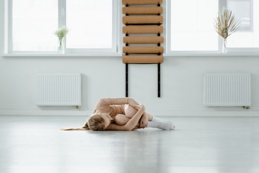 Young ballerina curled up in a serene, minimalist dance studio setting, showcasing flexibility.