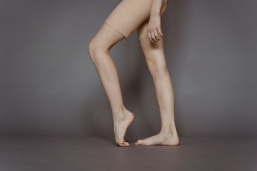 Free Unrecognizable barefoot female dancer wearing beige shorts bending foot while standing on gray background in modern light studio during practice Stock Photo