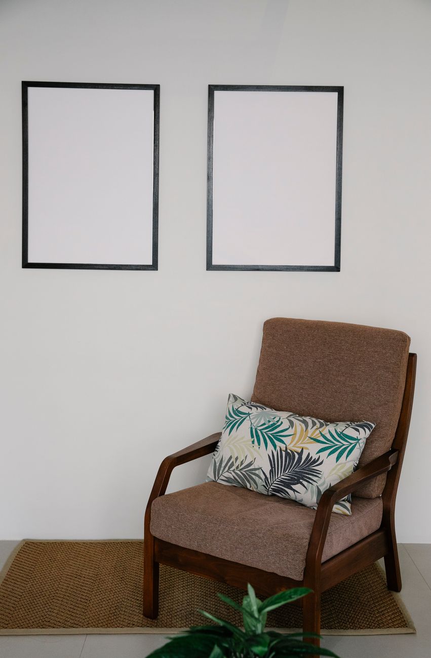 Cozy armchair with tropical cushion beside blank picture frames in a minimalist room.