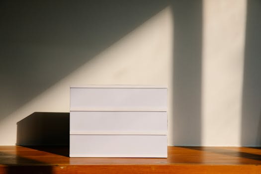 A minimalist white box with dramatic shadows cast on a wooden table in natural light.