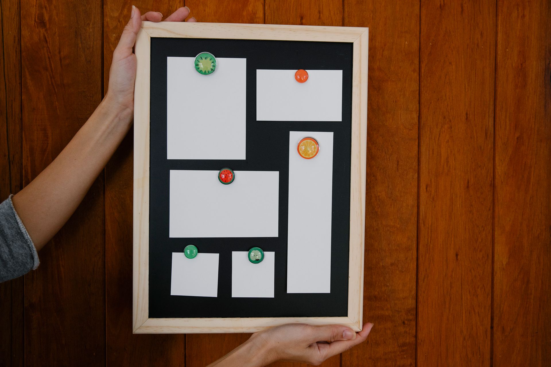 Hands holding a blank memo board with colorful magnets on a wooden wall background.