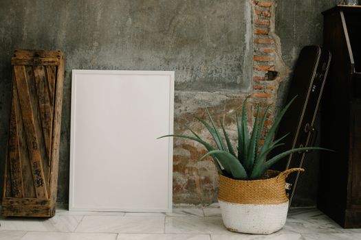 A rustic interior with blank frame, succulent, and wooden crate on concrete wall.