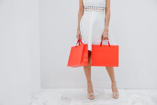Woman in a white dress holds orange shopping bags, showcasing fashion and style.