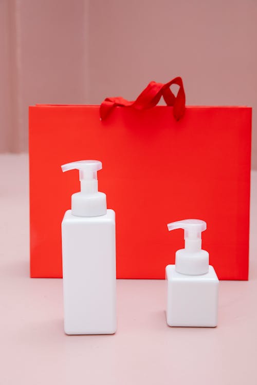 Big and Small Soap Dispenser on the Background of a Red Gift Bag 