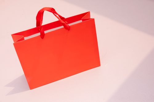 Free Vibrant orange paper shopping bag on a light pastel surface. Perfect for retail and branding visuals. Stock Photo