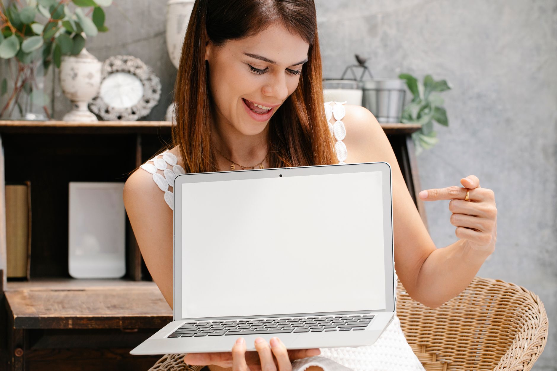 Young woman holding and pointing at a laptop with a blank screen, ideal for mockups.