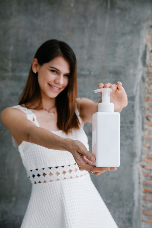 Free Woman in white dress smiling while holding a dispenser bottle. Stock Photo