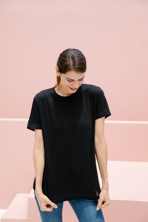 Free Young timid female with brown hair in black t shirt standing against stairs on pastel background Stock Photo