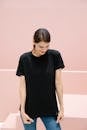 Young timid female with brown hair in black t shirt standing against stairs on pastel background