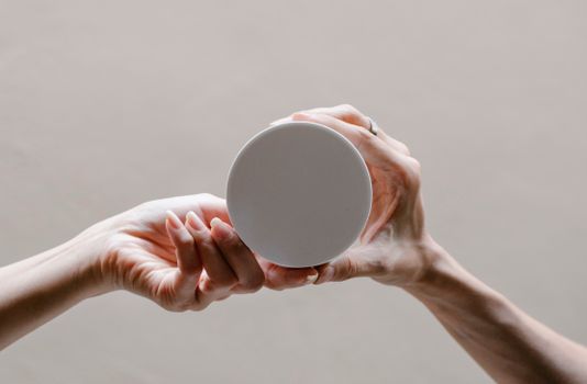 Crop unrecognizable women demonstrating round shaped plastic lid with smooth surface on gray background