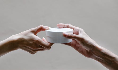 Crop woman passing jar of cream to girlfriend