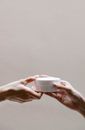 Crop anonymous female receiving glass jar of nourishing cream from girlfriend on gray background
