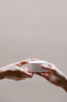 Crop anonymous female receiving glass jar of nourishing cream from girlfriend on gray background
