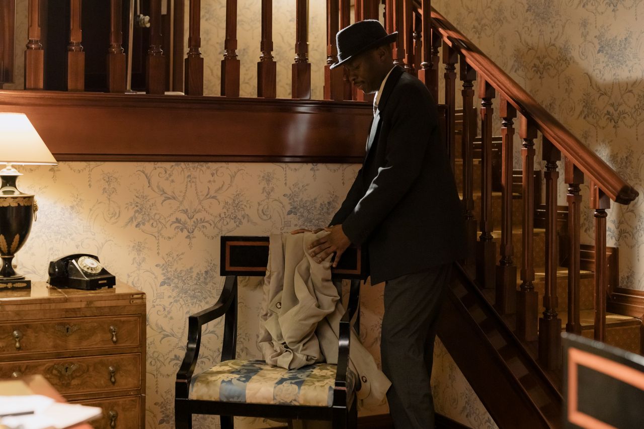 detective in a fedora hat in a retro styled room by the stairs