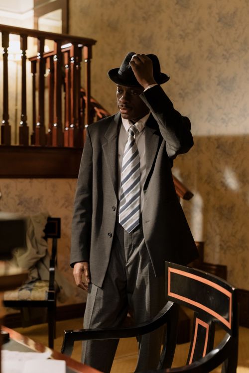 Free Stylish detective in a vintage setting wearing a fedora and suit, embodying a classic noir vibe. Stock Photo