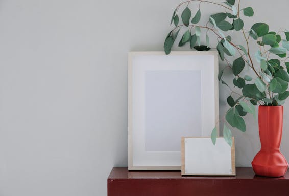 Wooden frame with white mockup placed on shelf near elegant vase with fresh green leaves