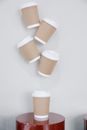 Collection of similar cups of takeaway coffee with kraft papers placed on small round table and hanging on white wall