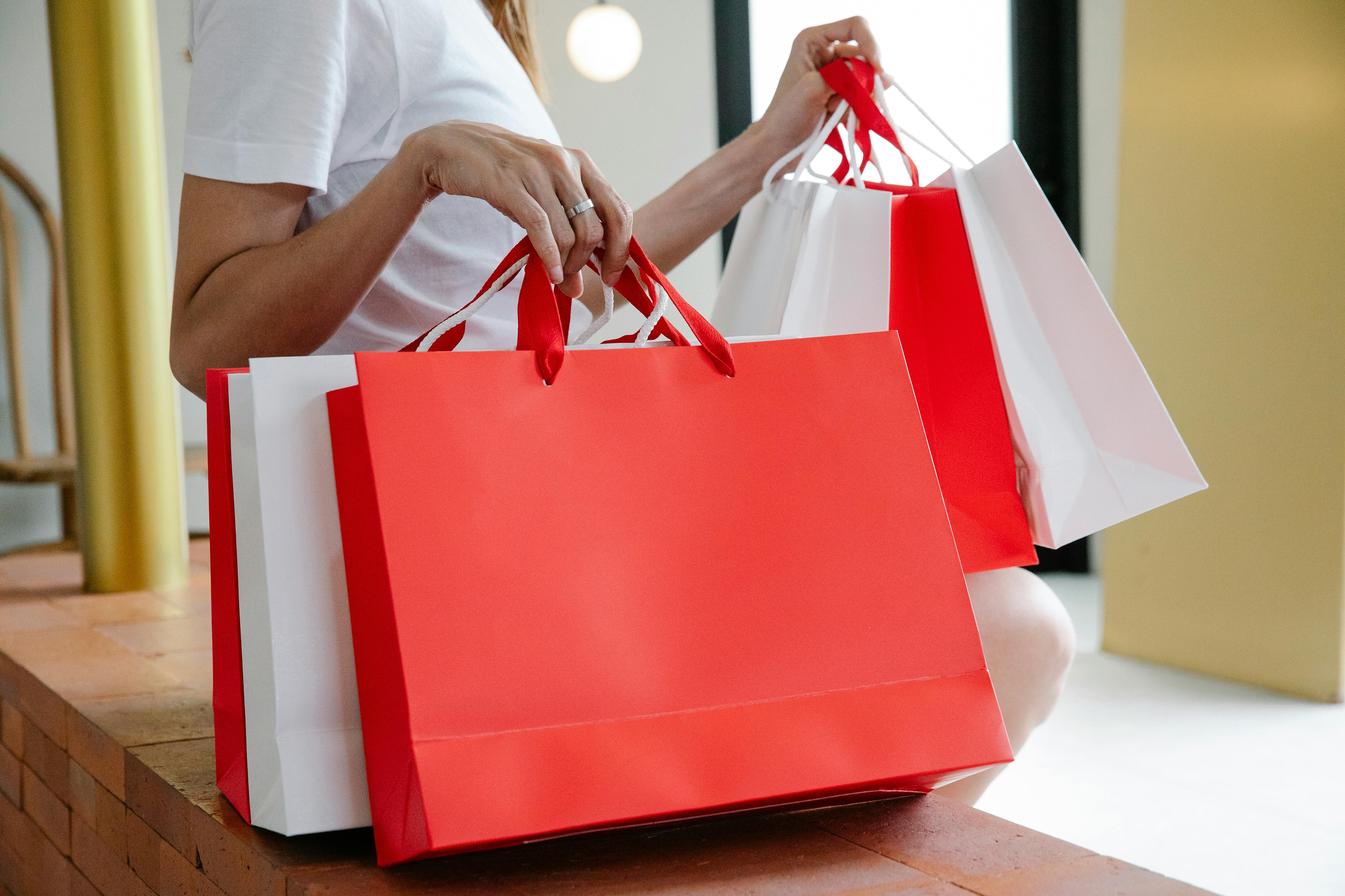 crop woman with white and red paper bags sitting on bench after shopping