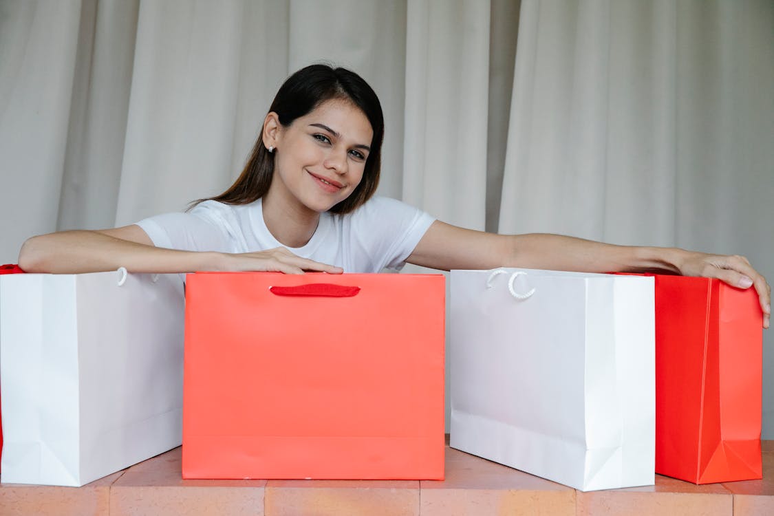 Free Delighted young woman showing purchases in paper bags and smiling Stock Photo