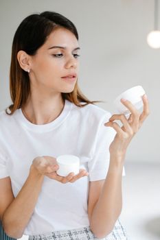 Confident young lady with ling dark hair in stylish outfit testing new skin care products in light studio