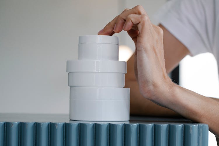 Crop Woman Touching Stack Of Blank Jars Of Various Creams