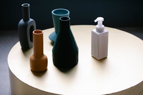 From above of white pump bottle of cosmetic lotion placed on round table near set of elegant vases of various shapes