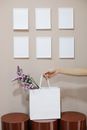 Crop anonymous female holding white shopping bag with bunch of fresh flowers near gray wall with set of frame mockups