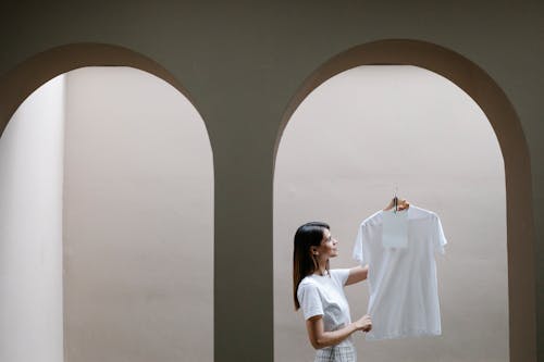 Stylish woman demonstrating t shirt on hanger near arched doorway