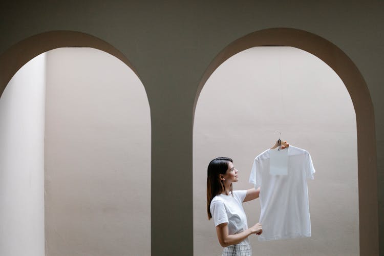 Stylish Woman Demonstrating T Shirt On Hanger Near Arched Doorway