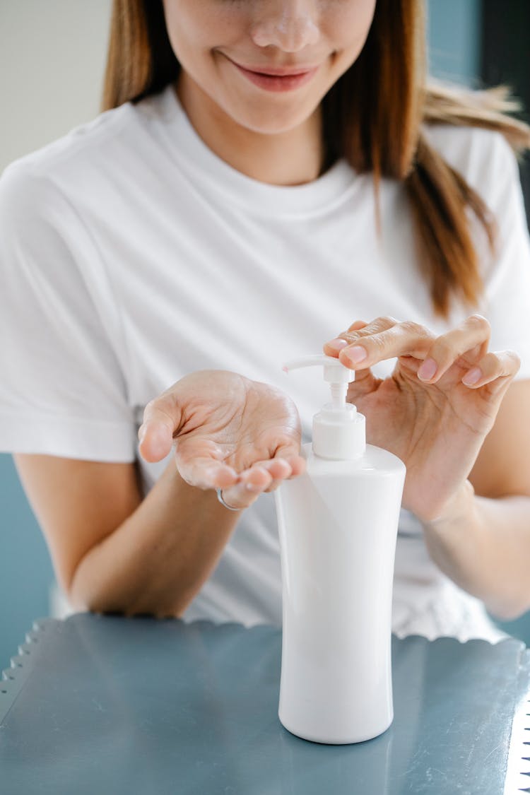 Crop Delighted Lady Applying Lotion From Pump Bottle During Cosmetic Procedure