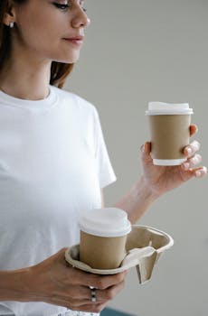 Woman holding eco-friendly coffee cups in a modern casual setting, promoting sustainability.