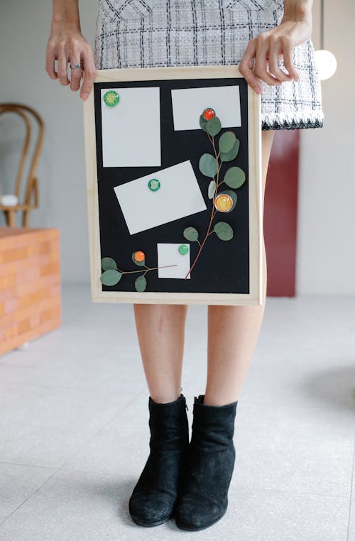 Unrecognizable female demonstrating blackboard with blank paper sheets and plant twigs in creative workplace