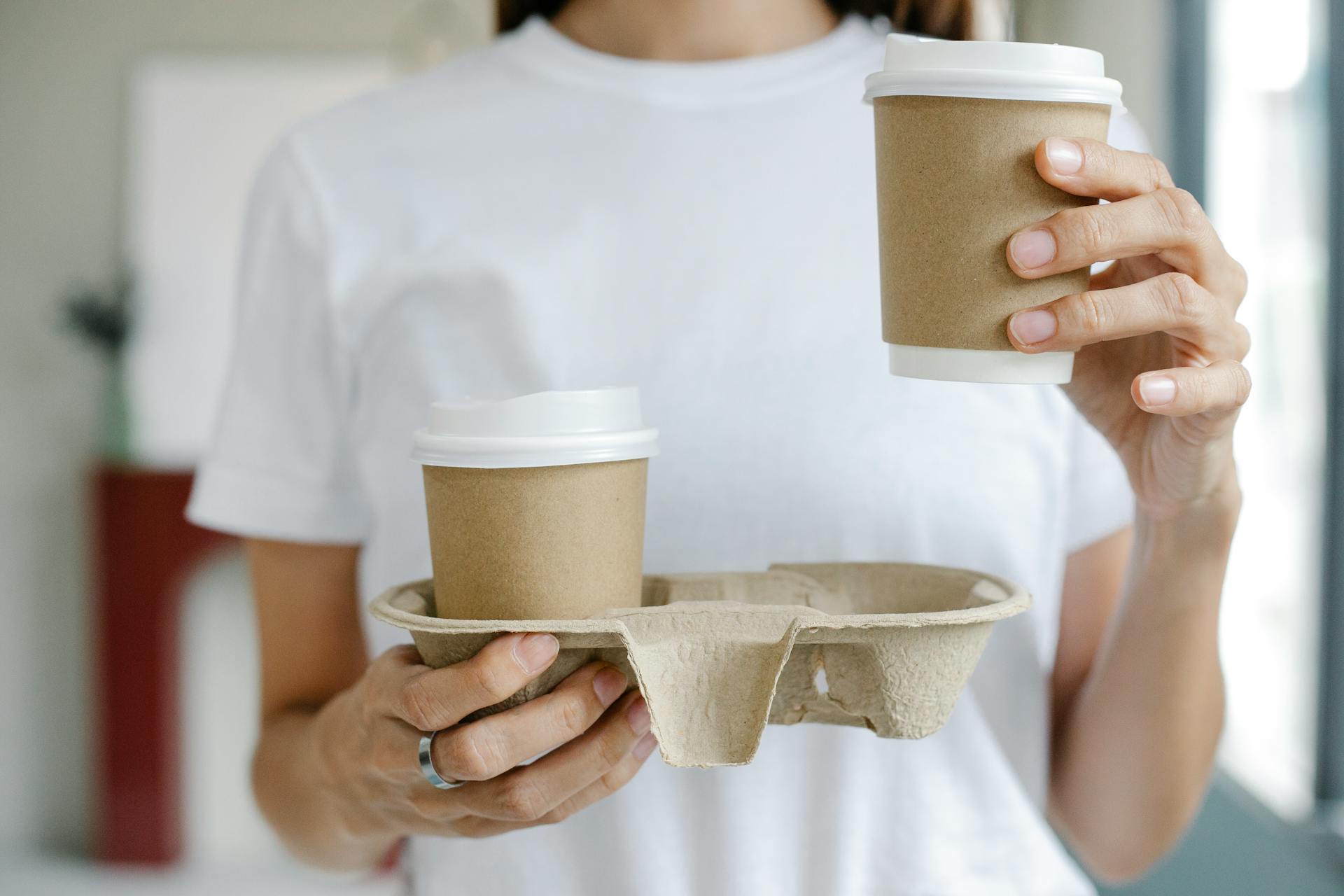 Woman holding eco-friendly coffee cups in a disposable holder, showcasing a modern and sustainable lifestyle.