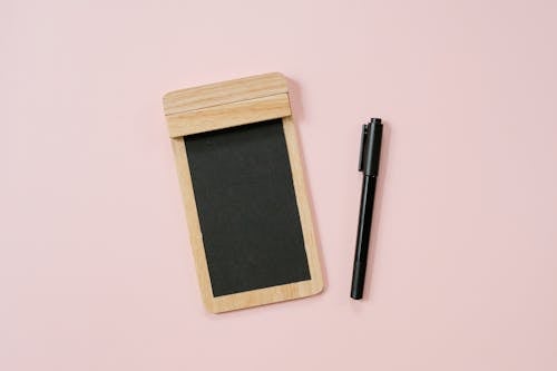Top view of pen and lumber notebook with black pages placed on pink background