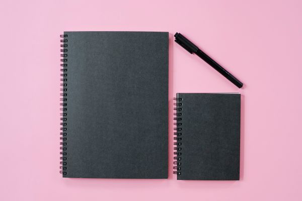 Notebooks and a pen arranged on a pink background
