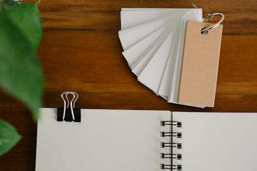 Top view of set of blank labels placed on wooden table near planner with paper clip