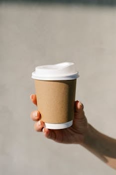 Minimalist photo of a hand holding an eco-friendly coffee cup against a gray background.