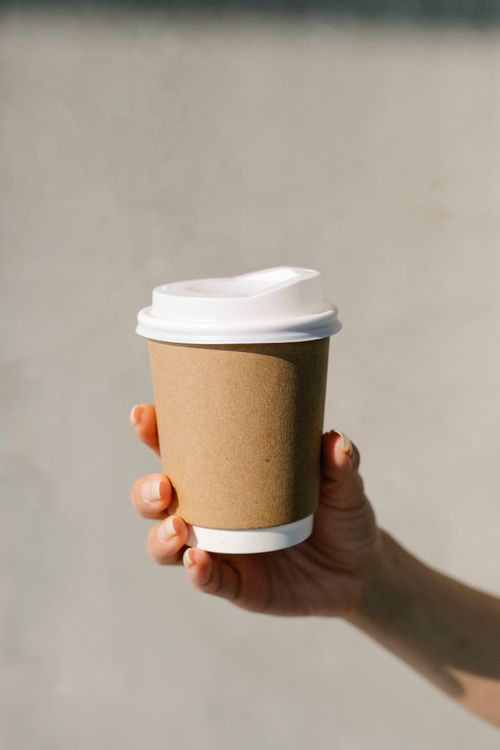 Free Unrecognizable female demonstrating paper cup of coffee to go against gray wall in morning Stock Photo