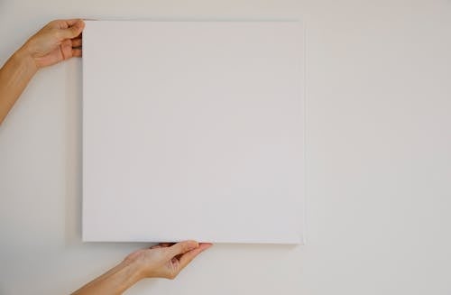 Free Unrecognizable female demonstrating empty poster of square shape during advertisement campaign against gray wall Stock Photo