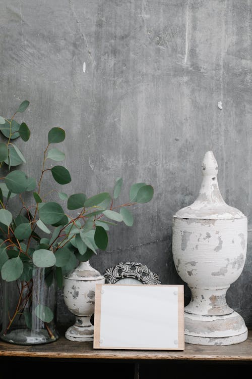 Free Board with blank paper sheet placed near shabby retro decorations and plant twigs against gray wall Stock Photo